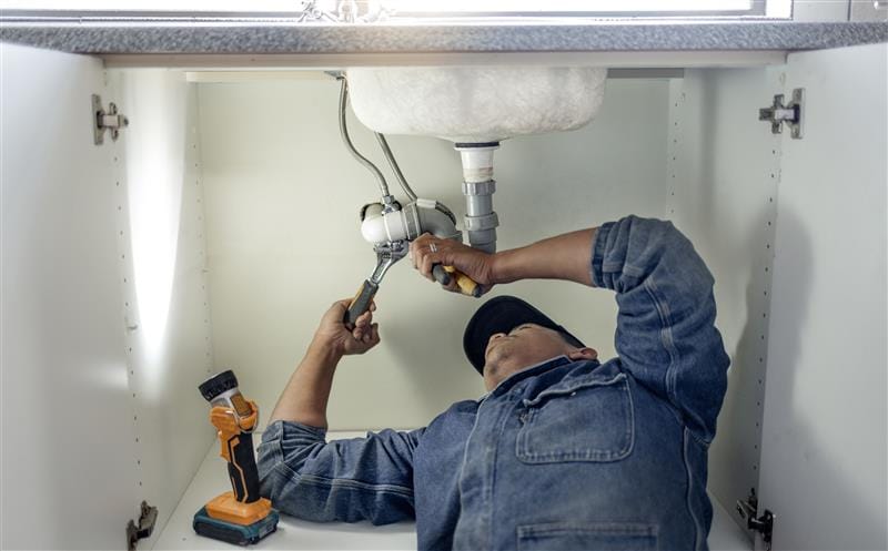 Plumber repairing pipes beneath a bathroom sink in Winter Springs