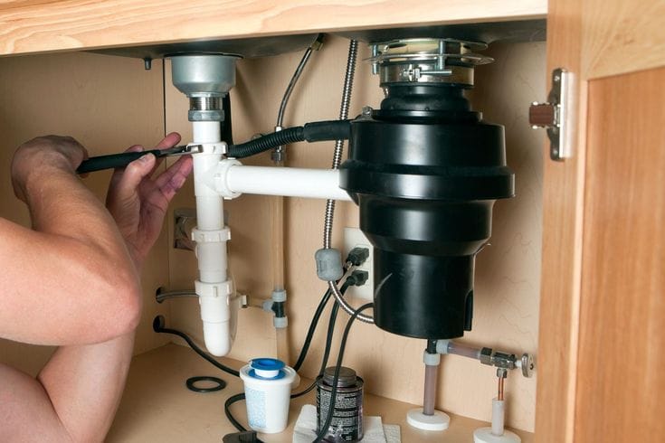 Plumber installing a garbage disposal beneath a kitchen sink in Winter Springs